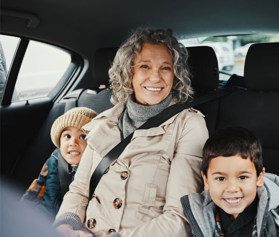 A woman and two children, belted in and smiling, in the back seat of a vehicle.
